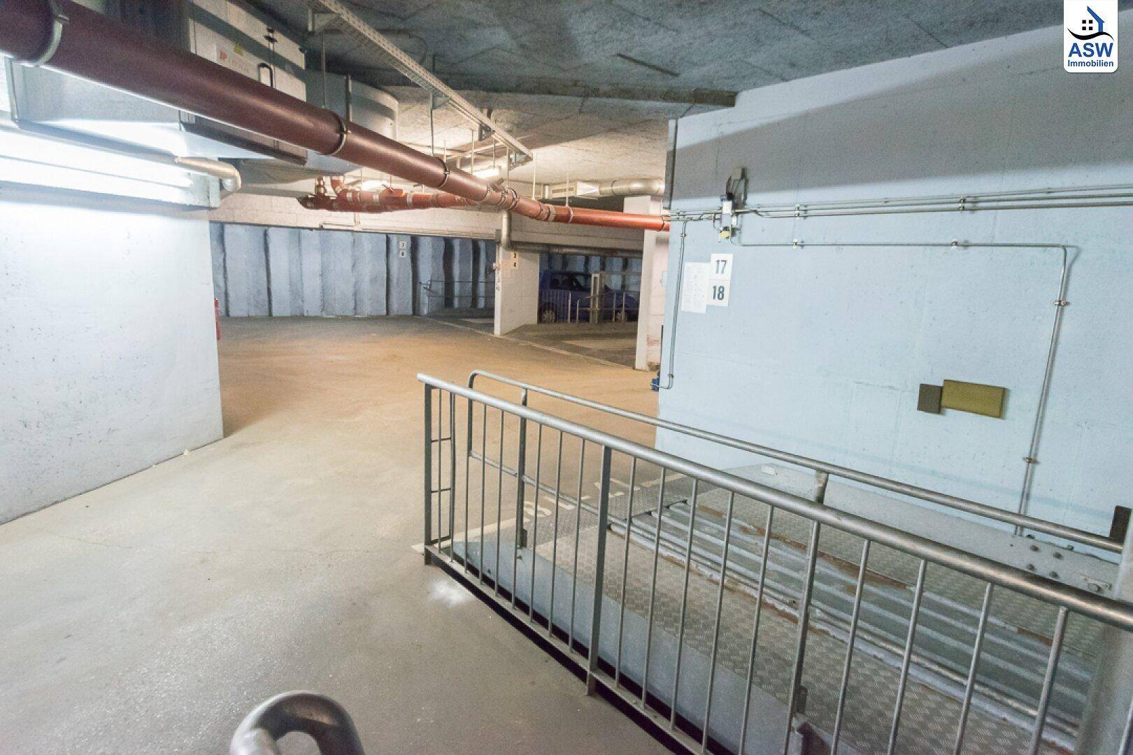 Tiefgarage mit einem Treppenabgang und sichtbaren Installationen an der Decke und Wänden.