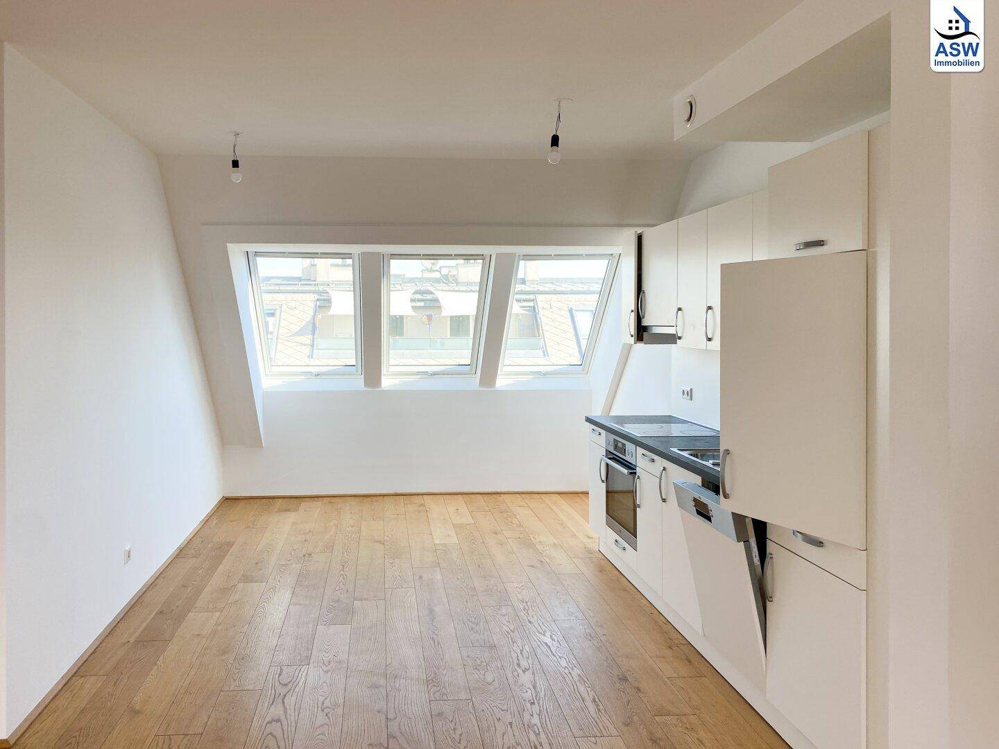 Heller Wohnraum mit integrierter Küchenzeile, Holzboden und schrägen Dachfenstern.