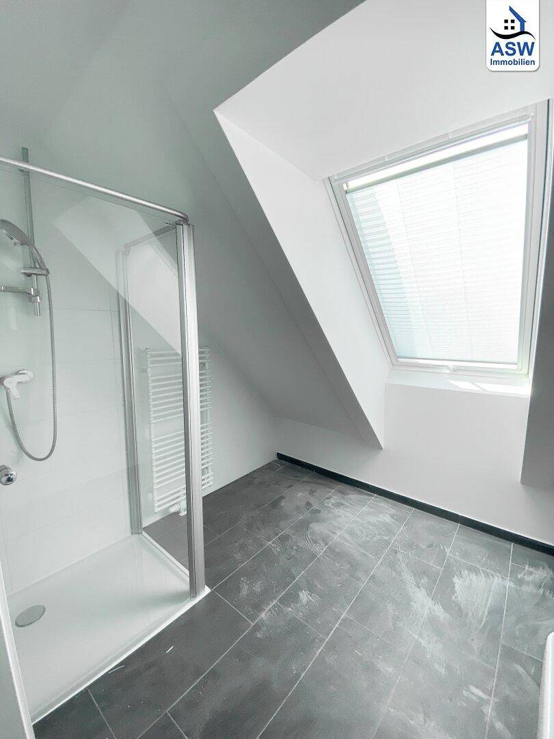Modernes Badezimmer mit Dusche, dunklen Fliesen und einem schrägen Dachfenster für Tageslicht.