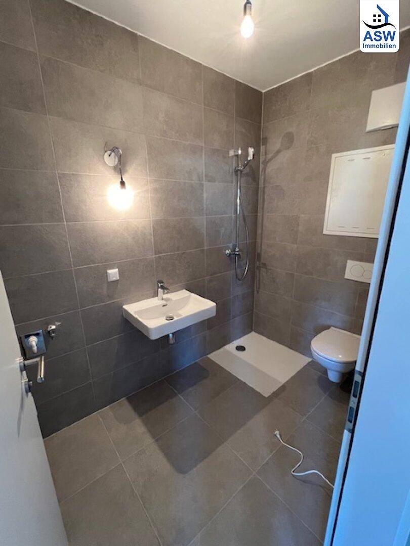 Modernes Badezimmer mit grauen Fliesen, wandhängendem WC und ebenerdiger Dusche.
