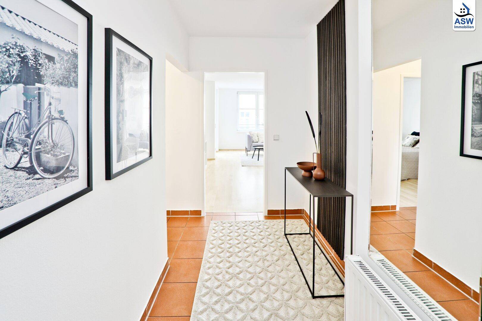 Heller Flur mit Terrakotta-Fliesenboden und modernem Konsolentisch, der zum Wohnbereich führt.