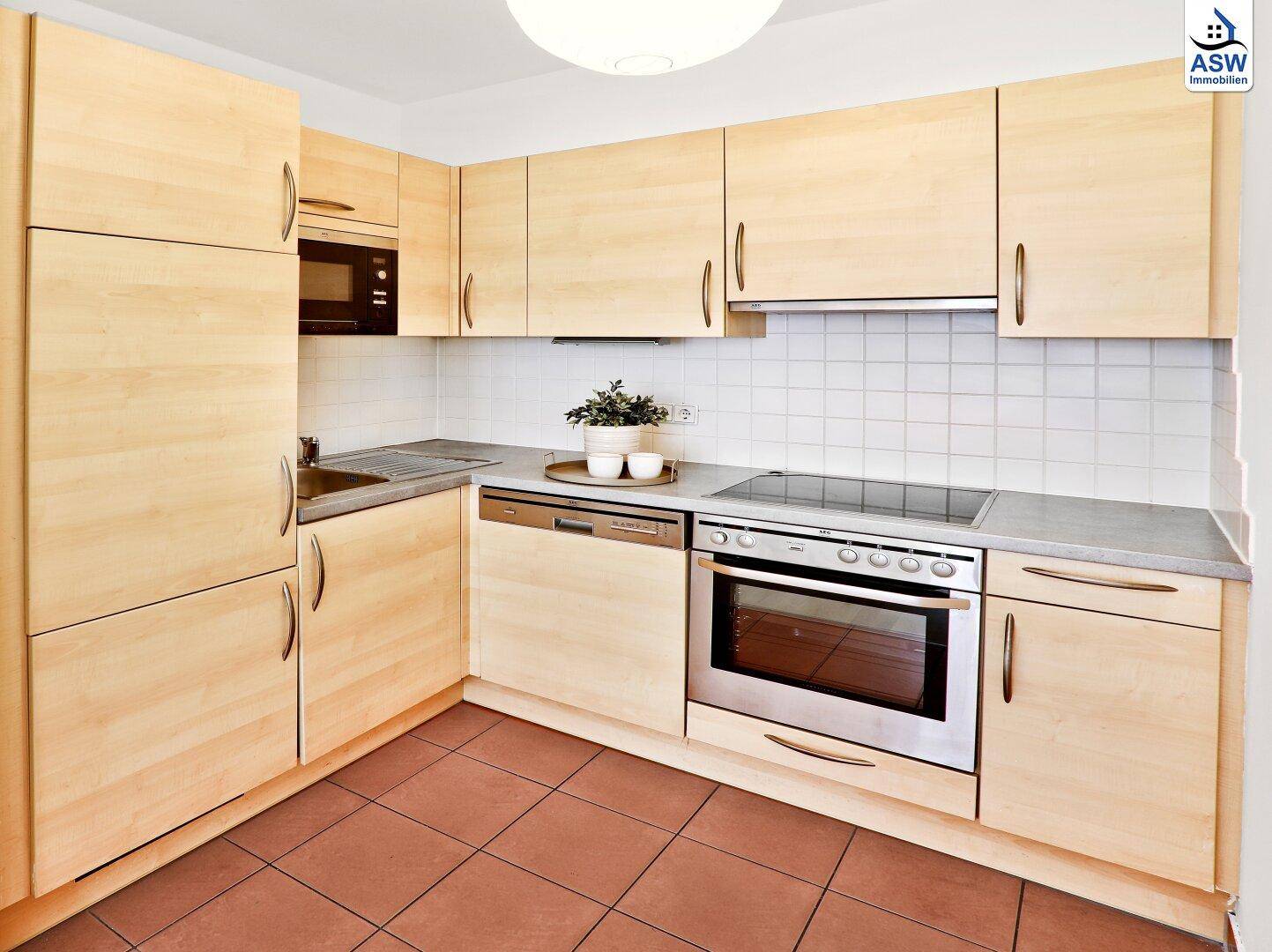 Funktionale Einbauküche mit hellen Holzfronten, modernen Geräten und Fliesenboden.