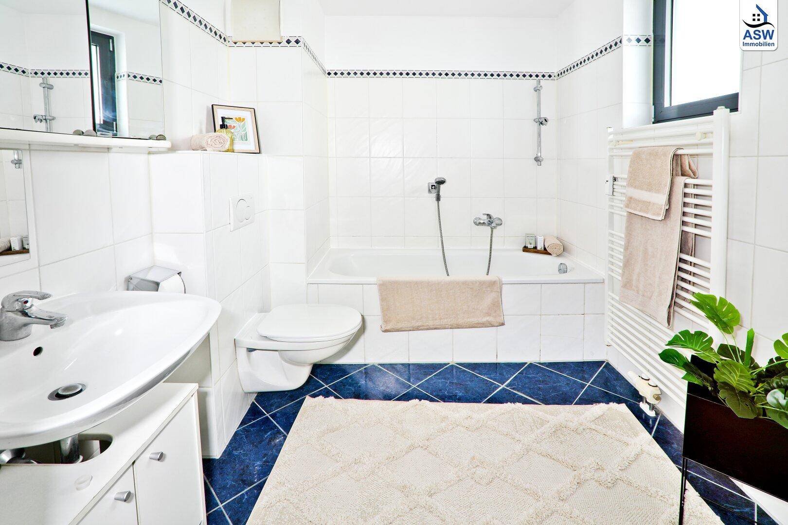 Gefliestes Badezimmer mit Badewanne, Waschbecken, WC und praktischem beheiztem Handtuchhalter.