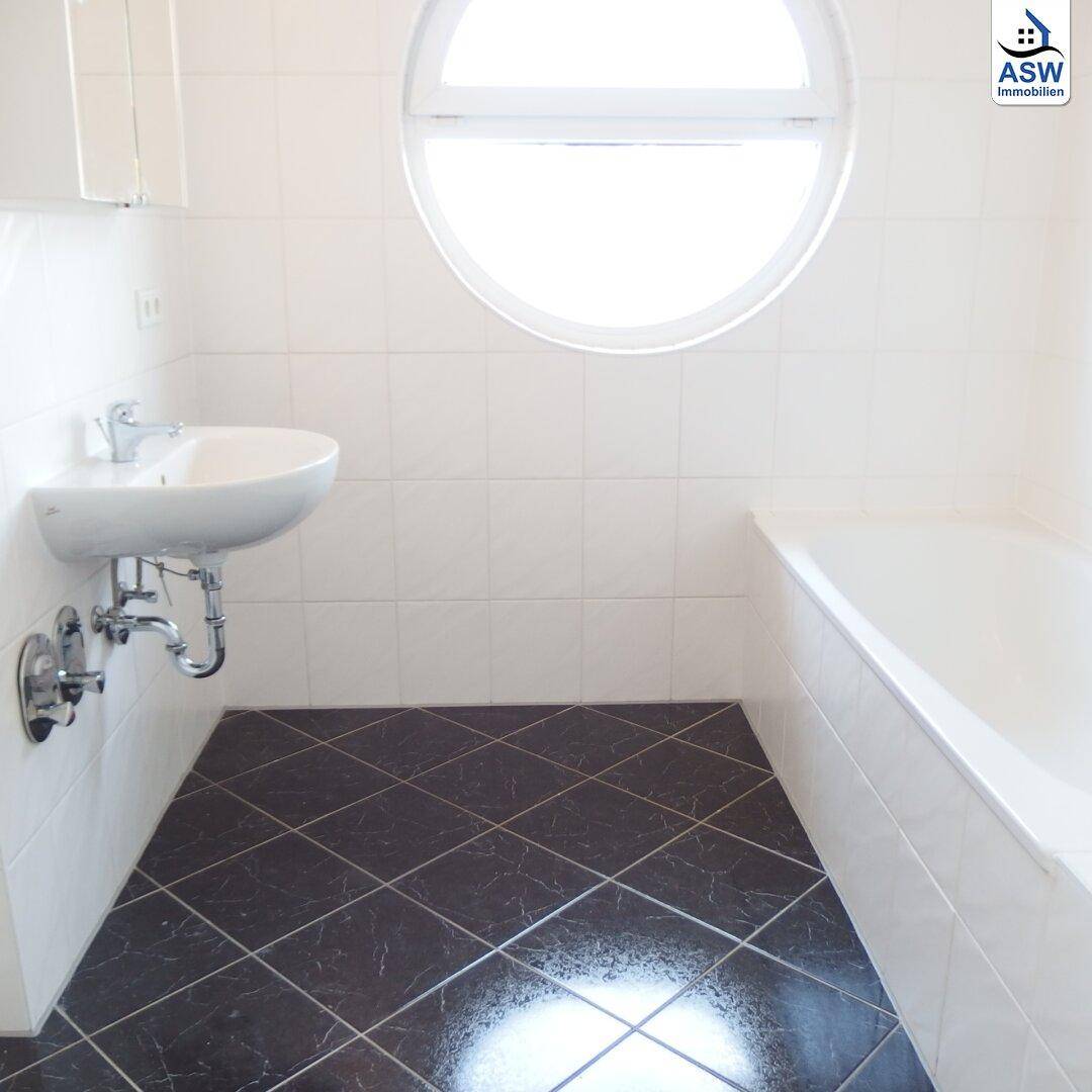 Helles Badezimmer mit Badewanne, Waschbecken und einem markanten runden Fenster.