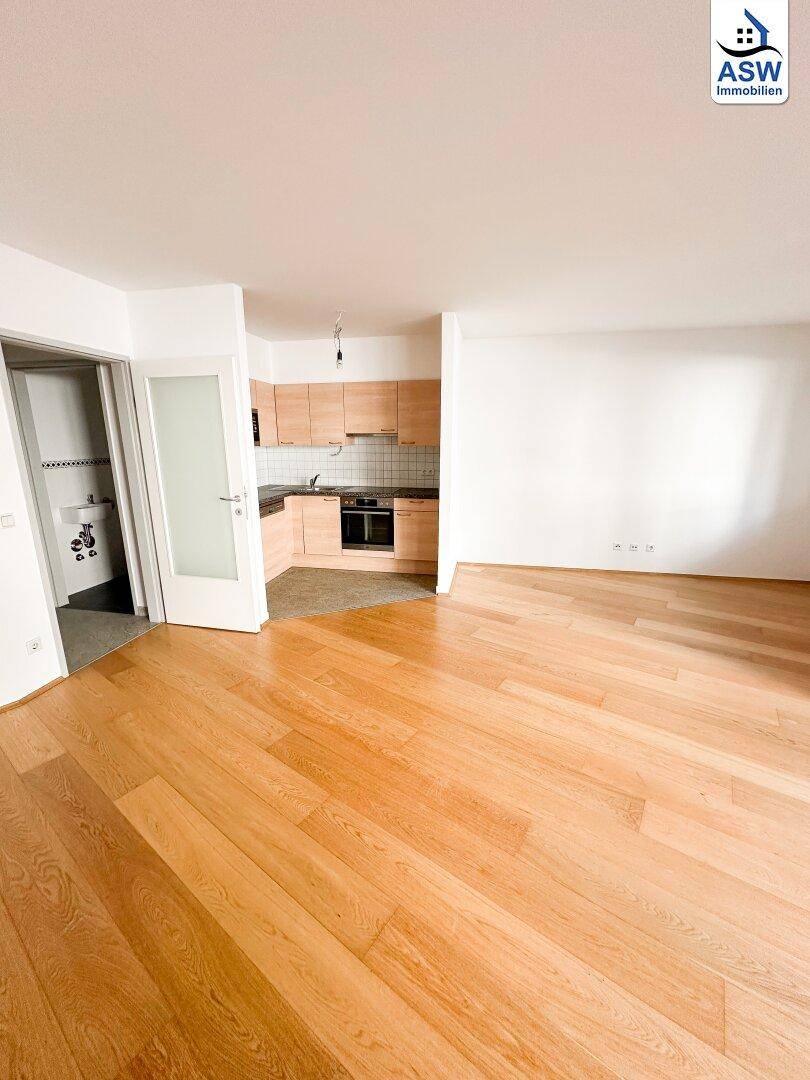 Offener Wohnbereich mit Holzfußboden und Blick auf die angrenzende Küchenzeile.