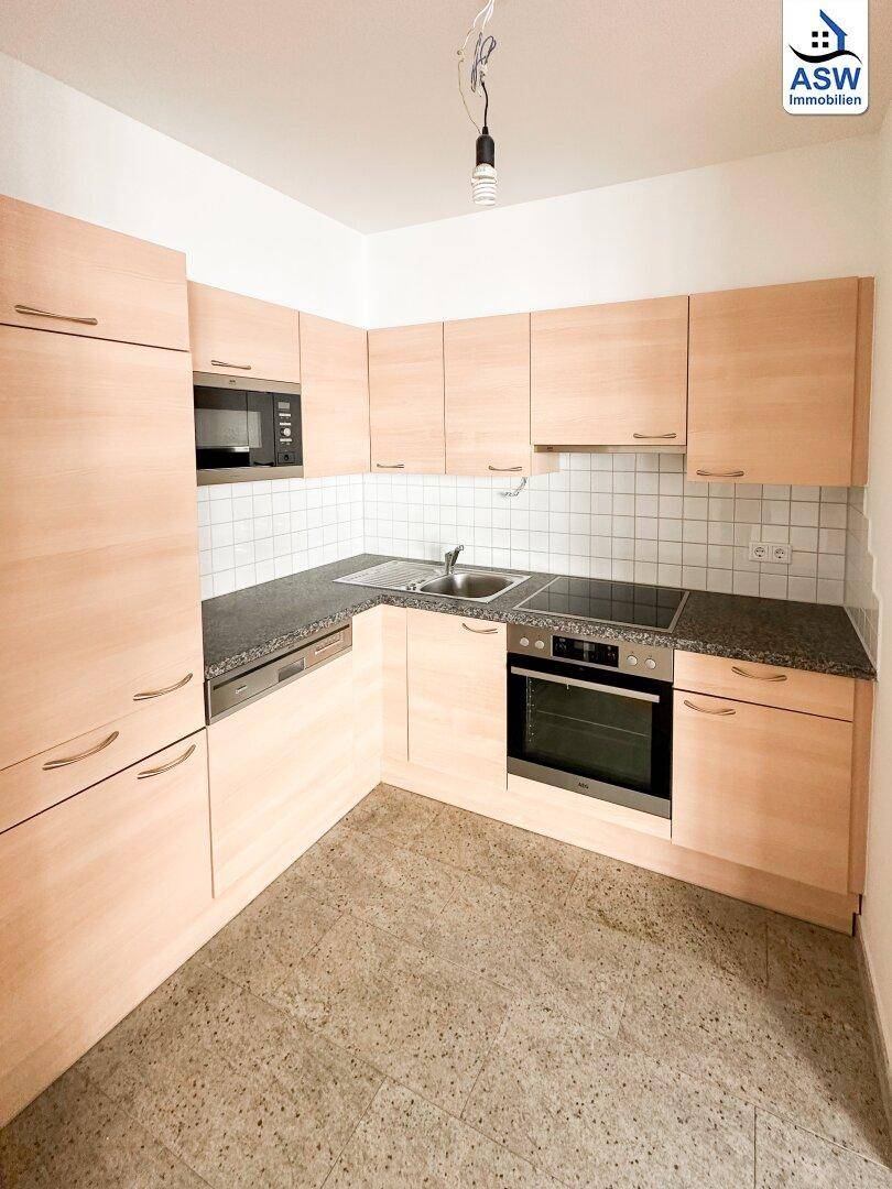 Funktionale Einbauküche mit hellen Holzfronten, dunkler Arbeitsplatte und Fliesenboden.