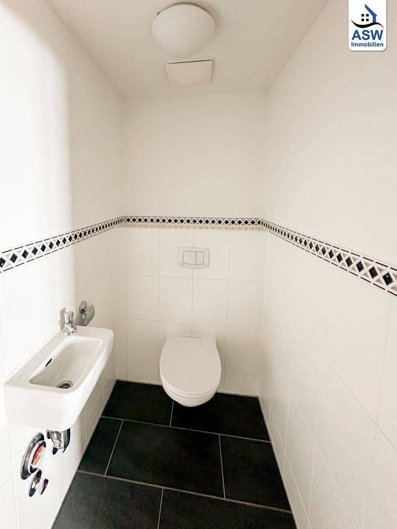 Modernes Gäste-WC mit Wand-WC, kleinem Waschbecken und dunklen Bodenfliesen.
