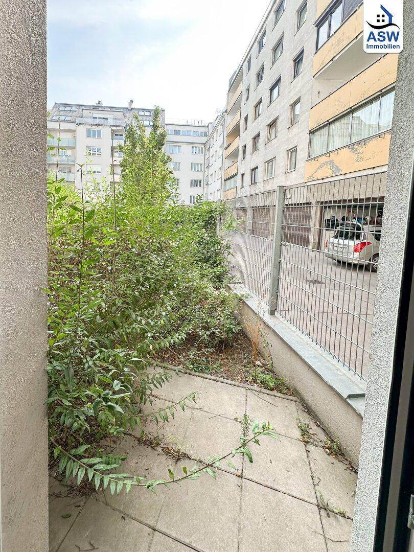 Kleiner, begrünter Außenbereich mit Zugang vom Wohnraum, umgeben von Gebäuden.