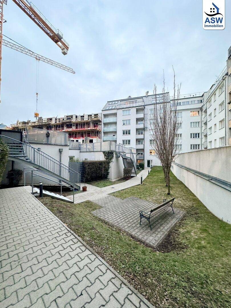 Gemeinschaftlicher Gartenbereich mit Sitzbänken und gepflasterten Wegen zwischen Wohngebäuden.