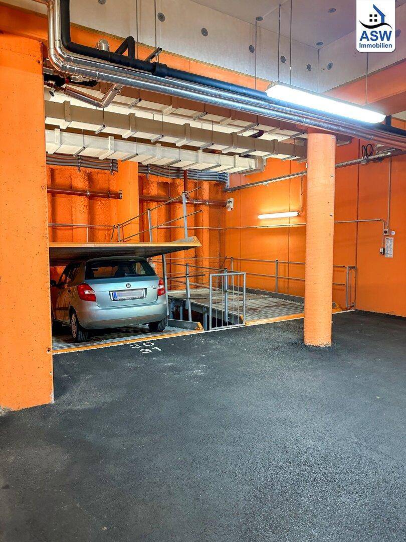 Tiefgarage mit orangefarbenen Säulen und einem Auto auf einer Hebebühne.