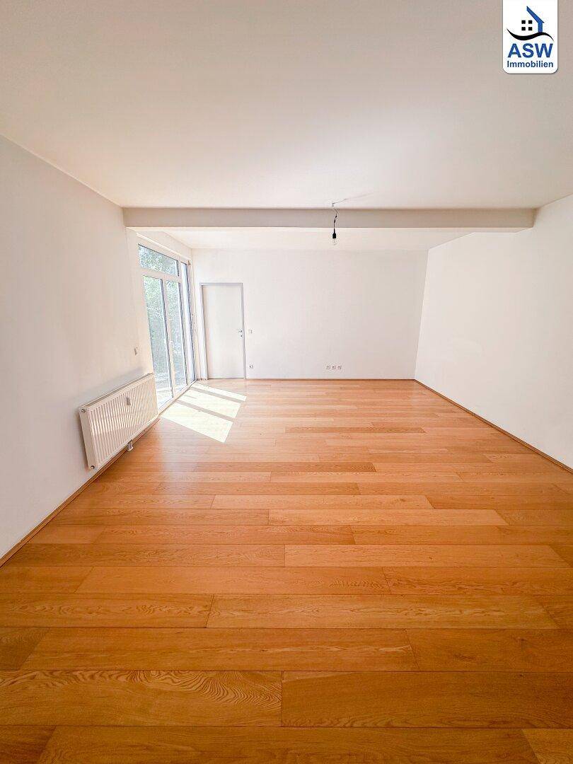 Geräumiges Wohnzimmer mit Parkettboden und viel Tageslicht durch große Fenster, bereit zur individuellen Gestaltung.