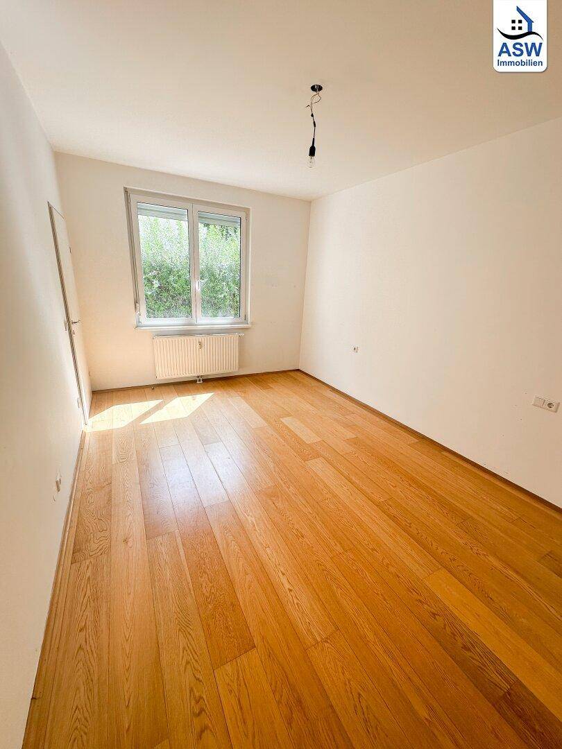 Helles Schlafzimmer mit Holzboden und Fenster mit Blick ins Grüne, bietet eine ruhige Atmosphäre.