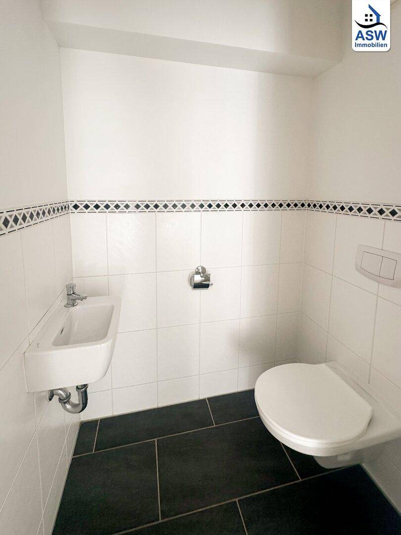 Modernes Gäste-WC mit dunklen Bodenfliesen und weißer Wandverkleidung, funktional und stilvoll.