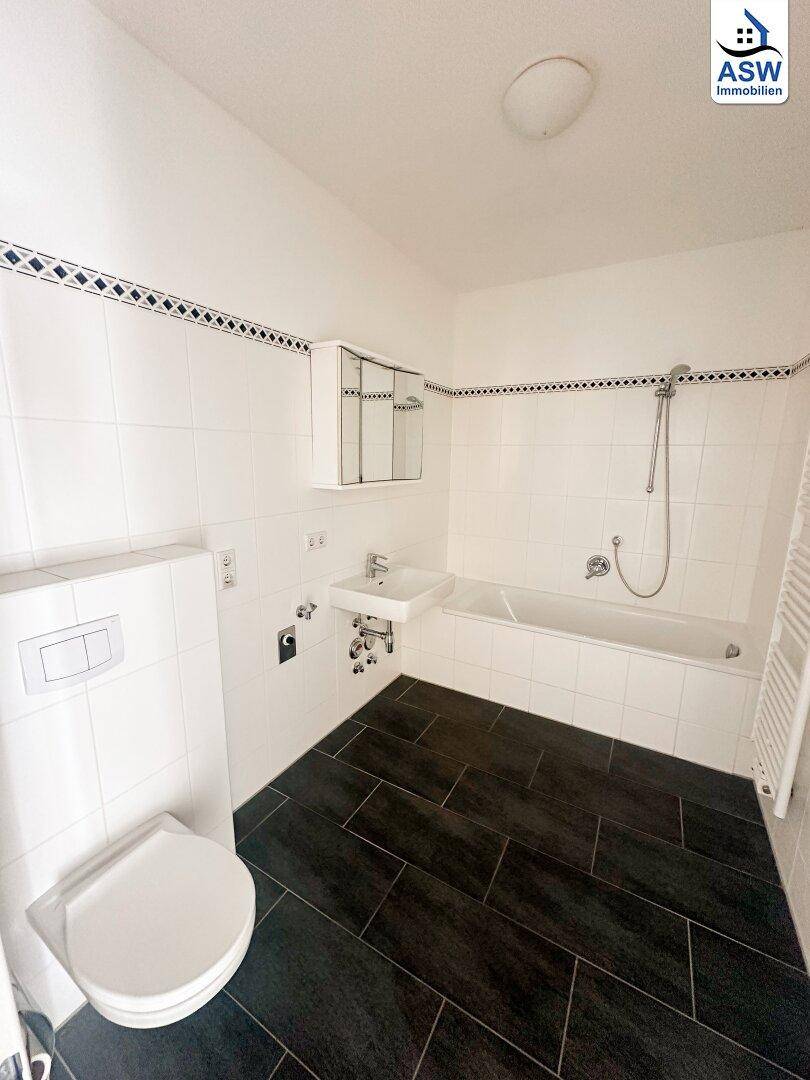 Badezimmer mit Badewanne, WC, Waschbecken und dunklen Bodenfliesen, bietet Komfort und Funktionalität.