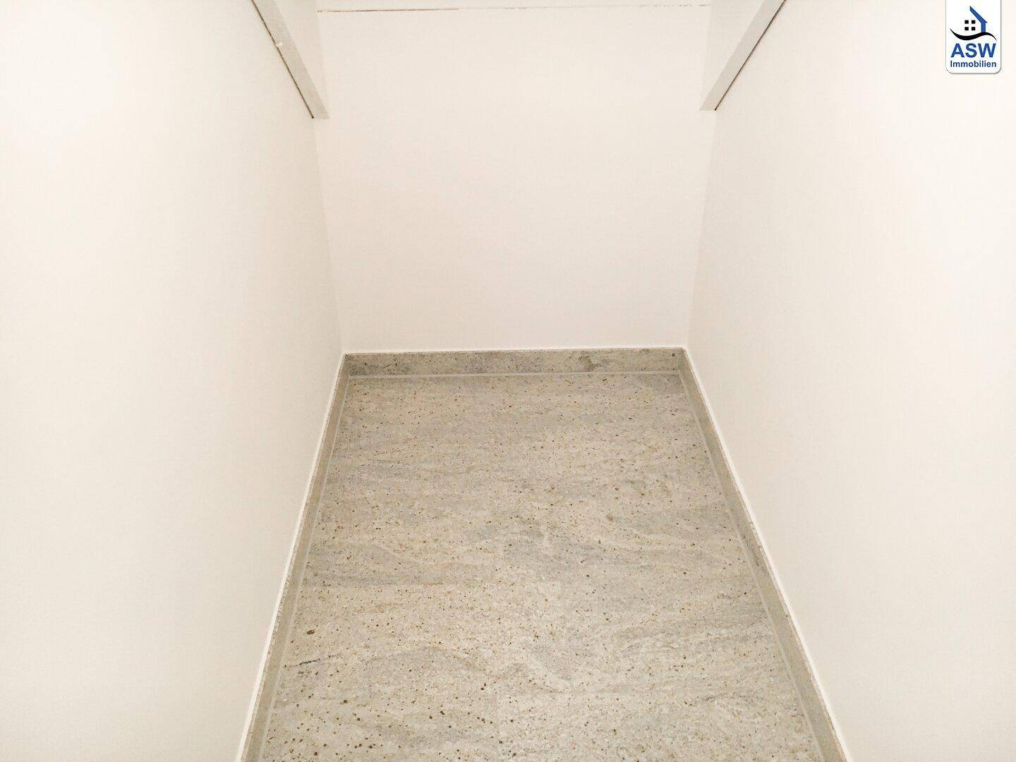 Kleiner Abstellraum mit weißen Wänden und grauem Fliesenboden.