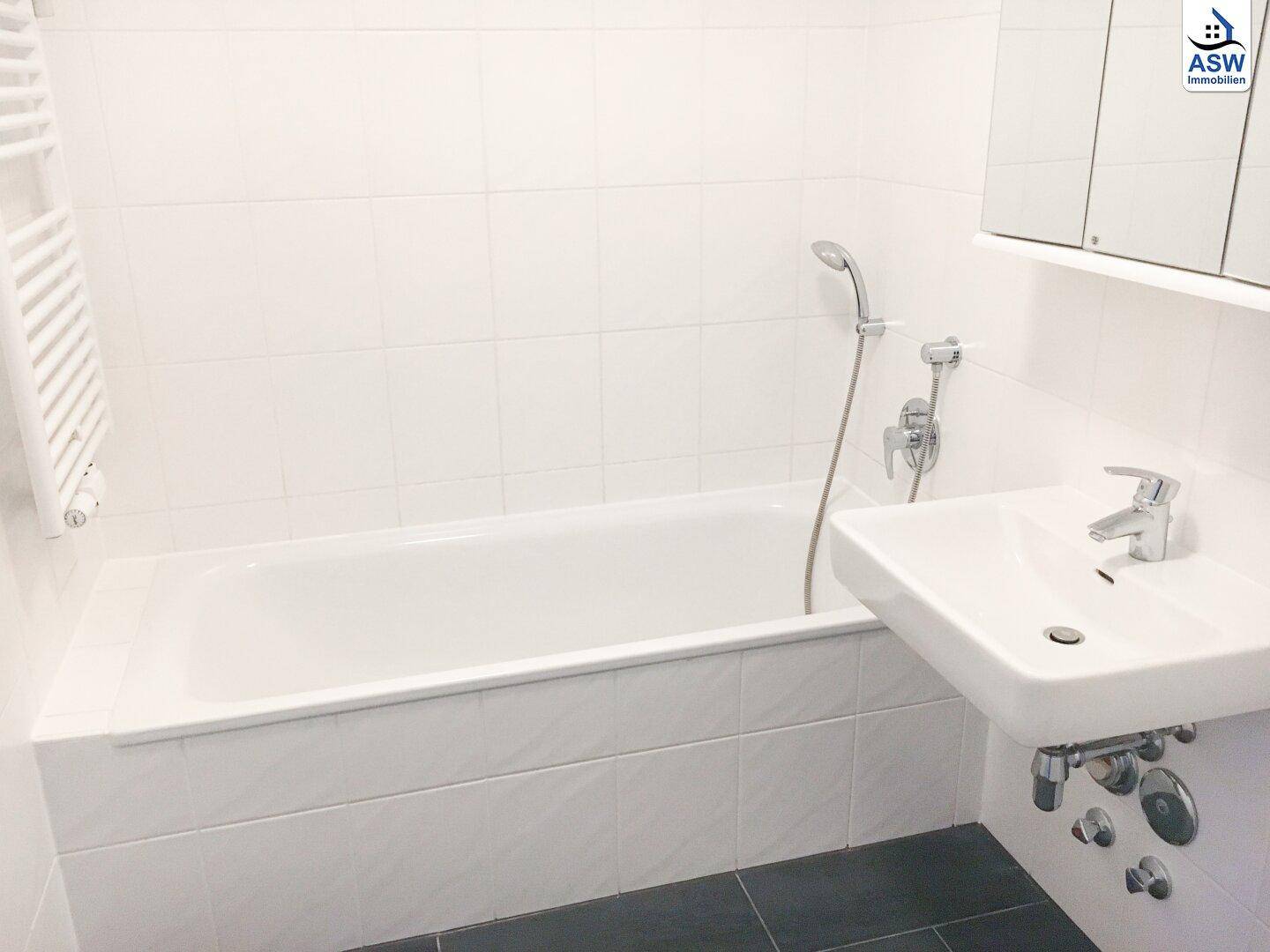 Modernes Badezimmer mit Badewanne, Waschbecken, weißen Wandfliesen und dunklem Boden.