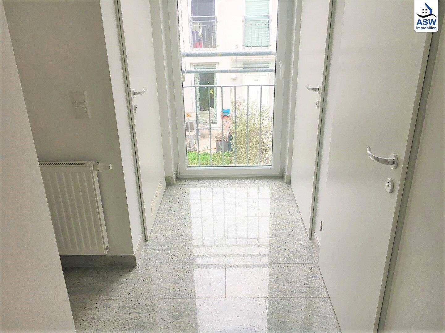 Flur mit grauem Fliesenboden, weißen Türen und einem Fenster mit Blick nach draußen.