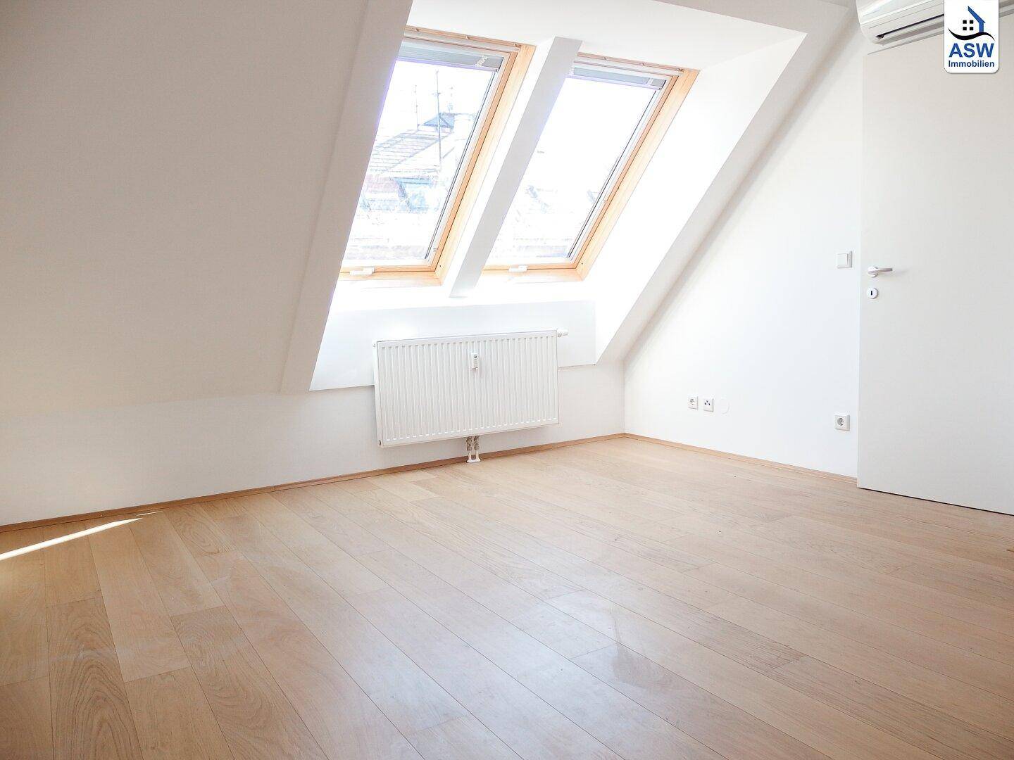Leeres Zimmer im Dachgeschoss mit zwei großen Dachfenstern und Heizkörper.