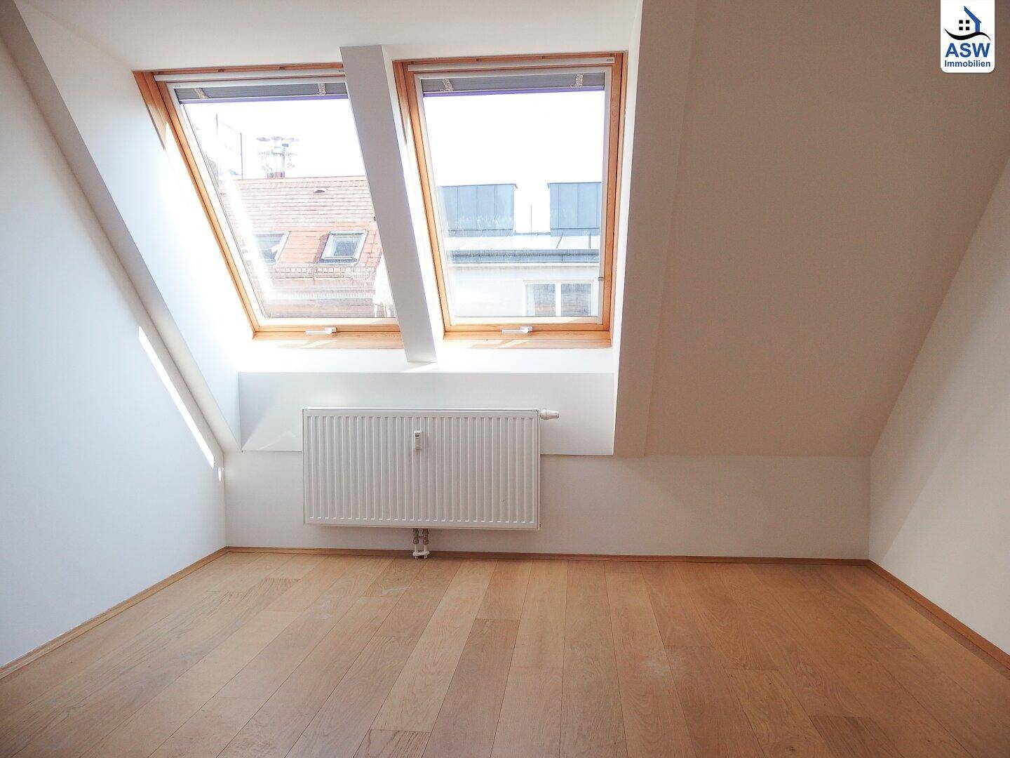 Dachgeschosszimmer mit schrägen Wänden, Holzboden und Blick durch die Dachfenster.