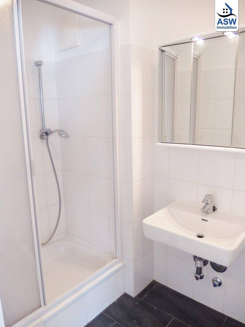 Modernes Badezimmer mit Dusche, Waschbecken und dunklen Fliesen.