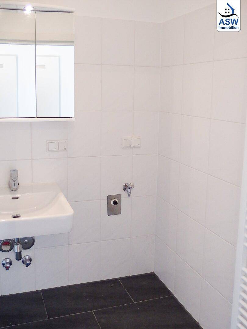 Badezimmer mit weißen Wandfliesen, Waschbecken und dunklem Fliesenboden.