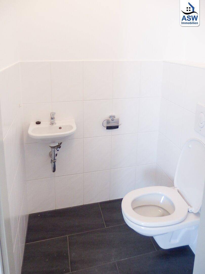 Separates WC mit Waschbecken und dunklem Fliesenboden, sauber und funktional.