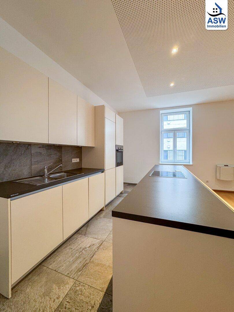 Moderne Einbauküche mit dunkler Arbeitsplatte, Spüle und integriertem Kochfeld in der Kücheninsel.