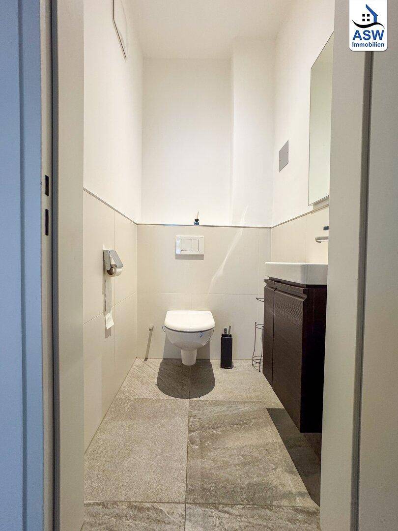 Modernes Gäste-WC mit wandhängender Toilette, kleinem Waschbecken und Fliesenboden.