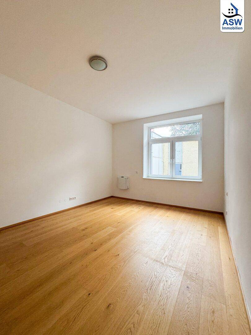 Helles Schlafzimmer mit schönem Holzboden und einem Fenster, das viel Tageslicht hereinlässt.