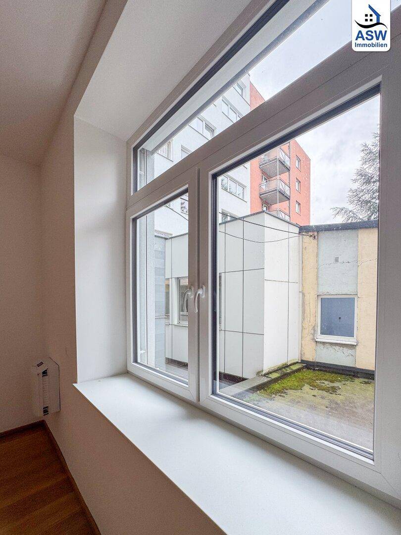 Blick aus dem Fenster auf einen Innenhof mit angrenzenden Gebäuden und etwas Grün.
