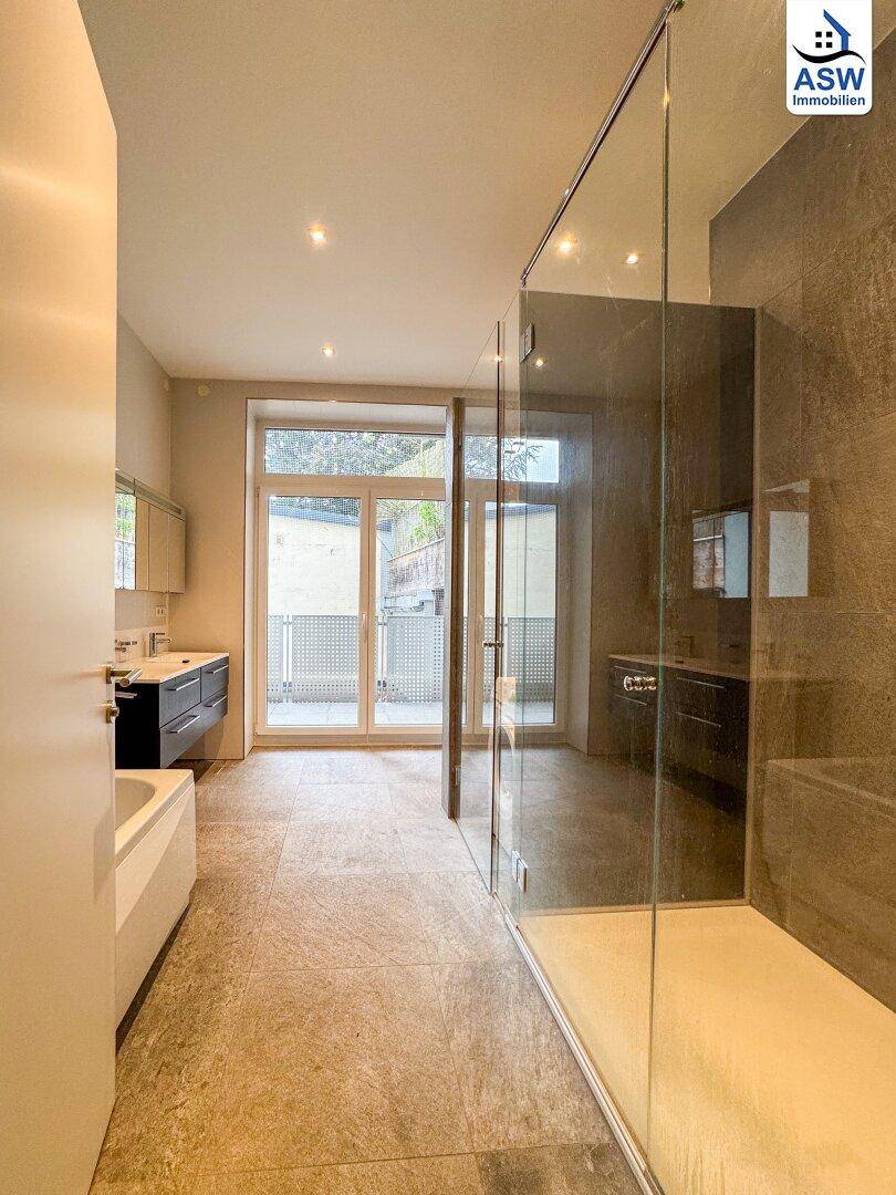 Geräumiges Badezimmer mit großer begehbarer Dusche, Badewanne und Zugang zu einem Außenbereich.