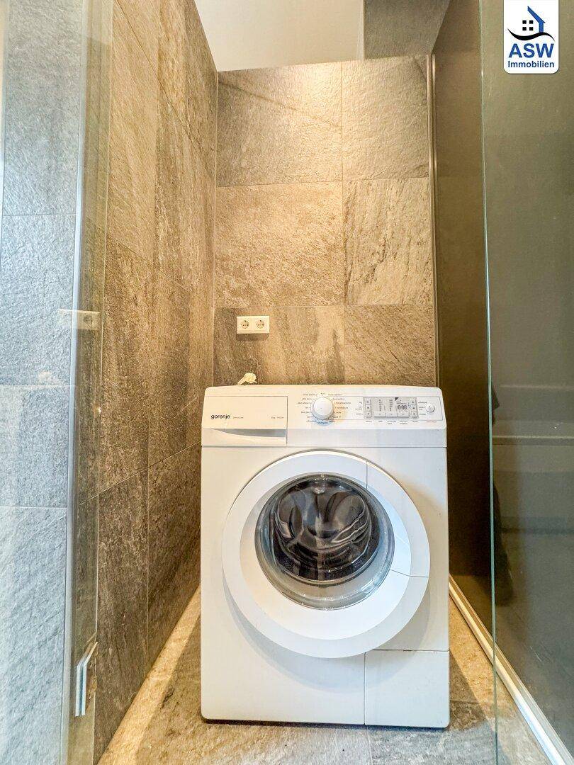 Waschmaschine in einem gefliesten Bereich, praktisch im Badezimmer integriert.