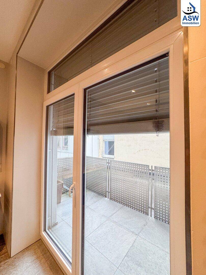 Blick von einem Innenraum durch eine große Fenstertür auf einen Balkon mit Metallgeländer.