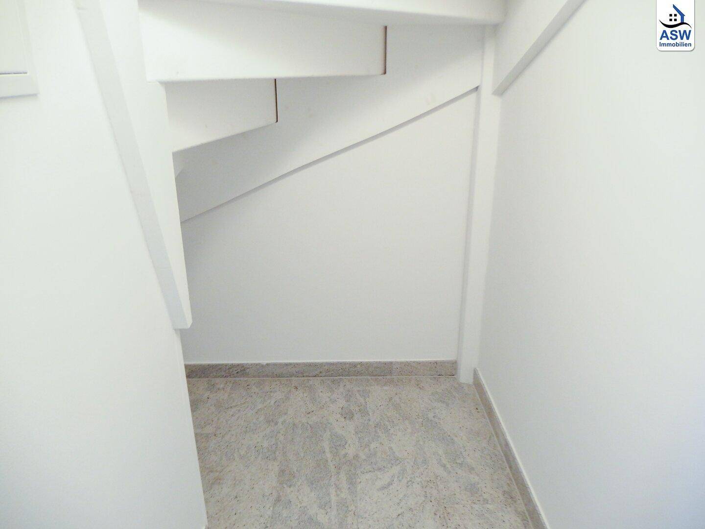 Blick von unten auf eine Treppe mit weißen Wänden und grau gefliestem Boden.