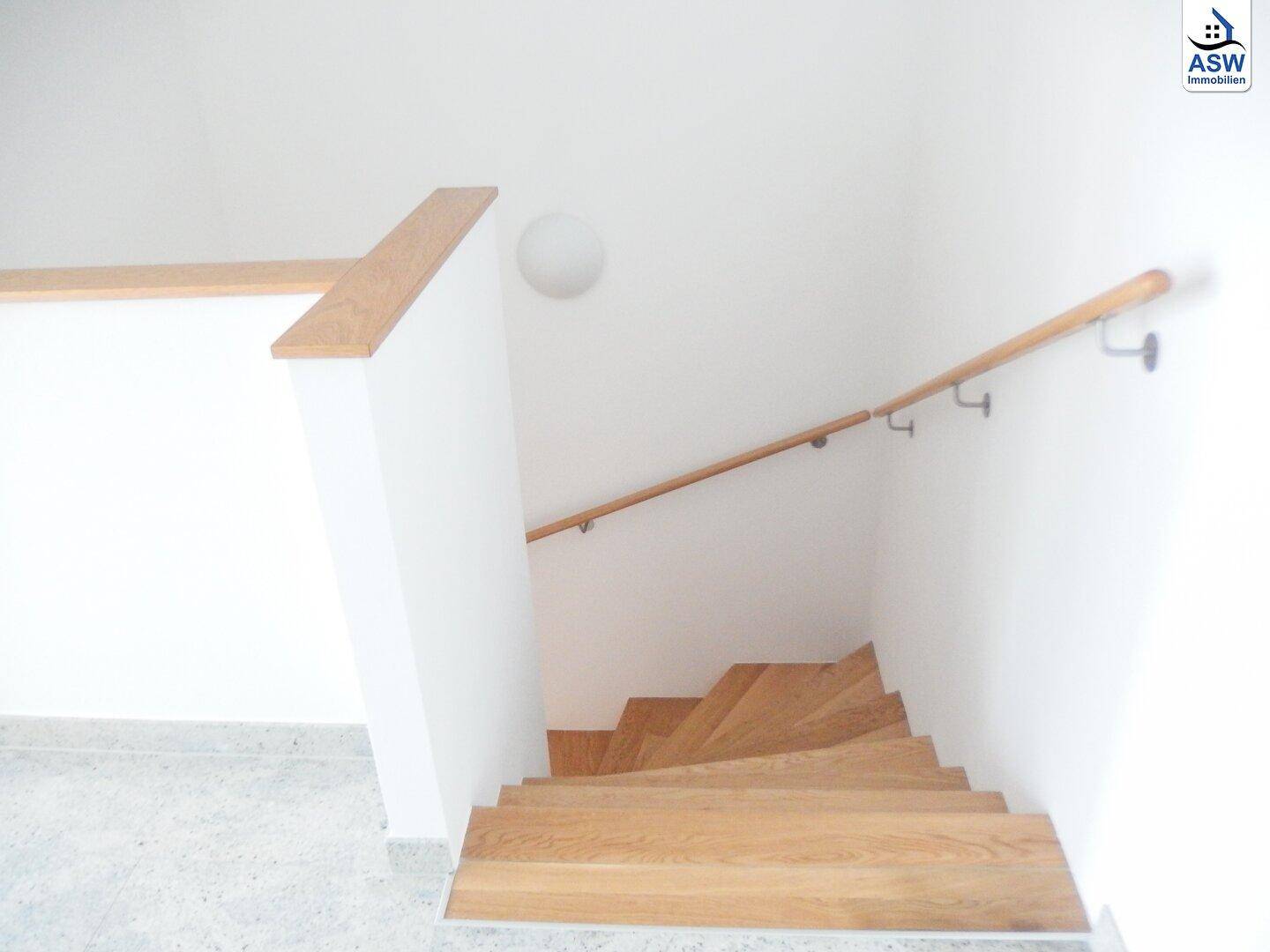 Holztreppe mit passendem Holzgeländer und weiß gestrichenen Wänden, gut beleuchtet.