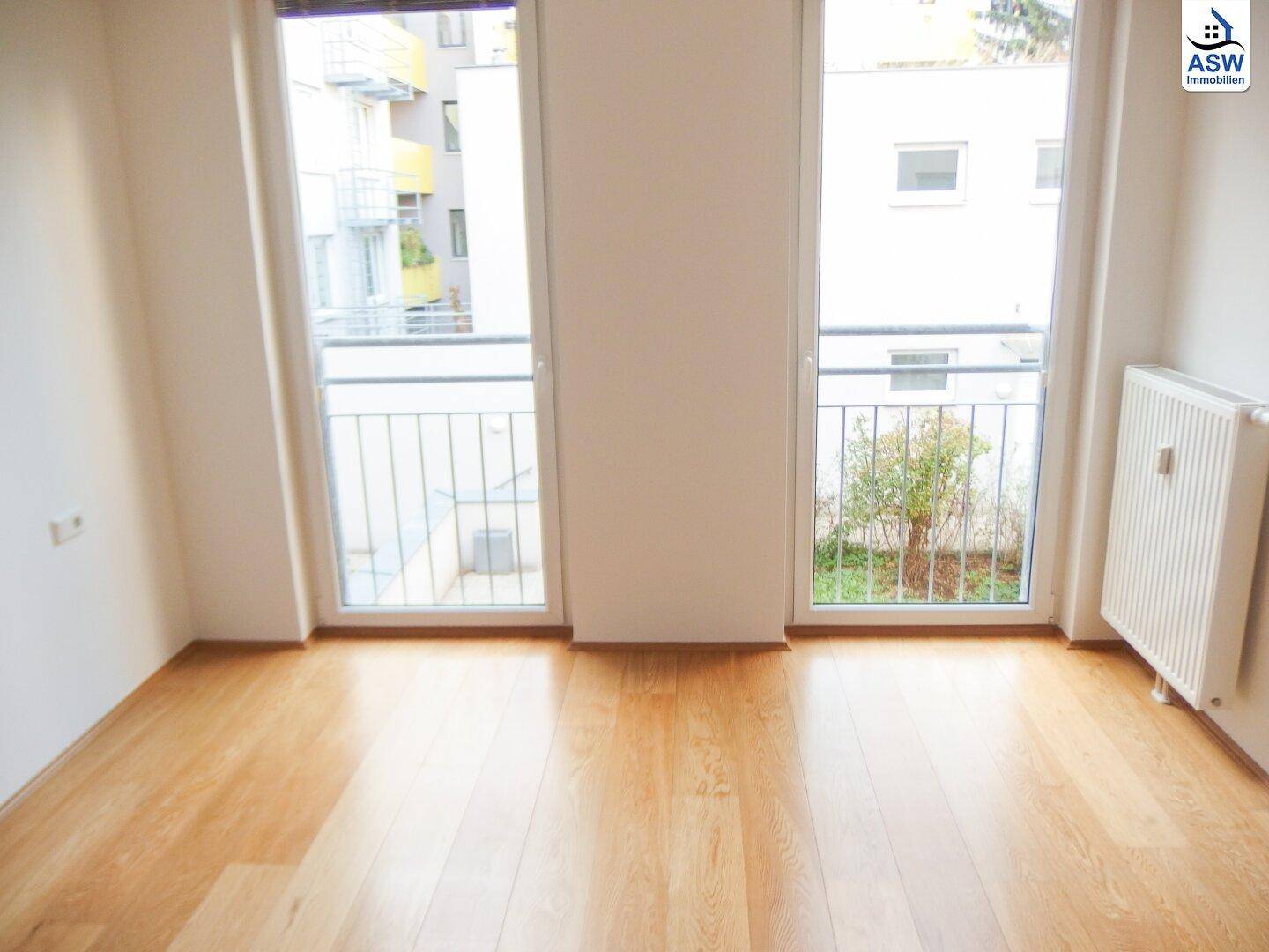 Geräumiges Zimmer mit Holzboden, weißen Wänden und zwei großen Fenstertüren mit Balkongeländer.