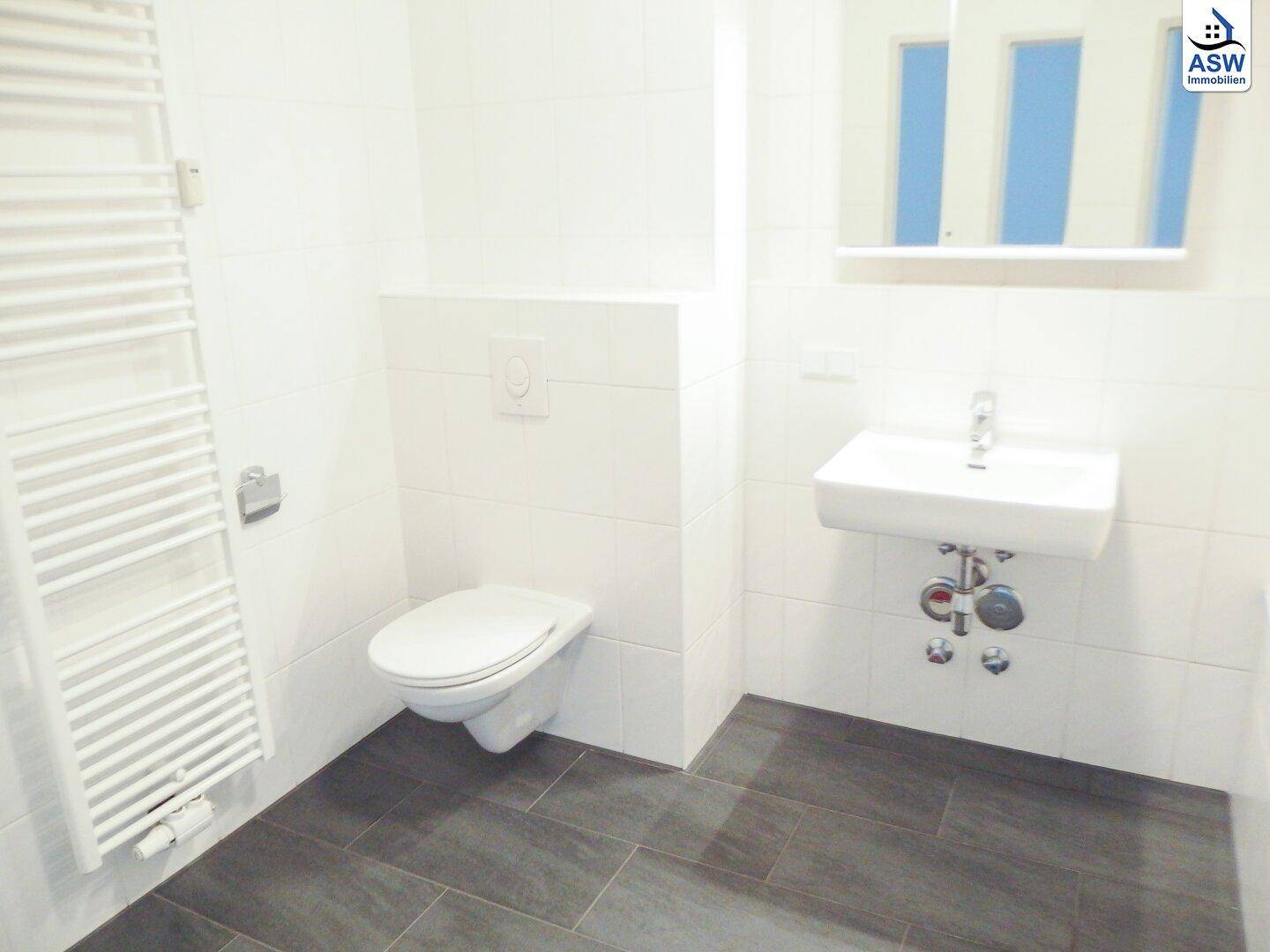 Modernes Badezimmer mit weißen Wandfliesen, dunklem Boden und wandhängendem WC sowie Handtuchheizkörper.