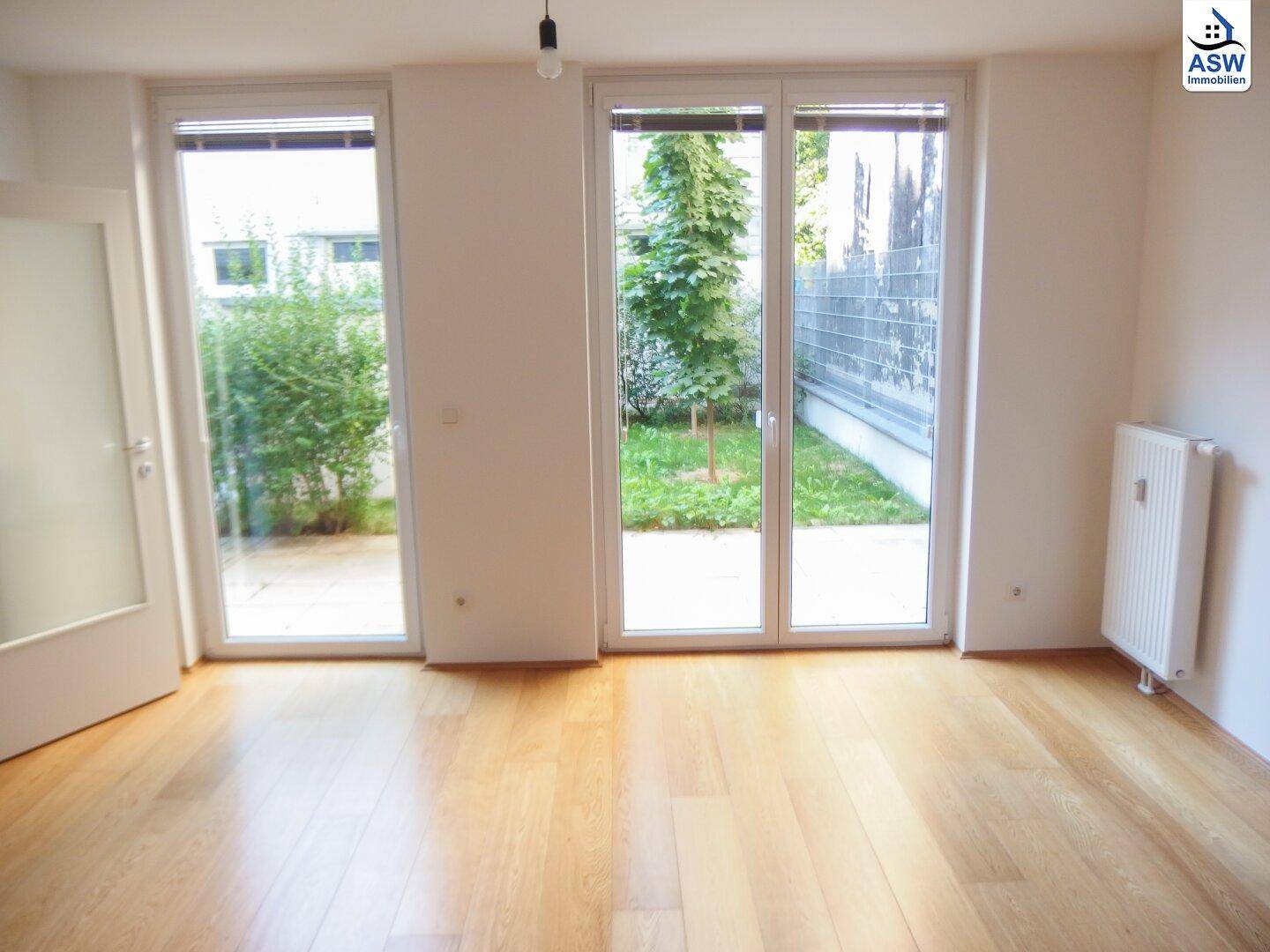 Heller Wohnraum mit Holzboden und großen Fenstertüren zum Gartenbereich.