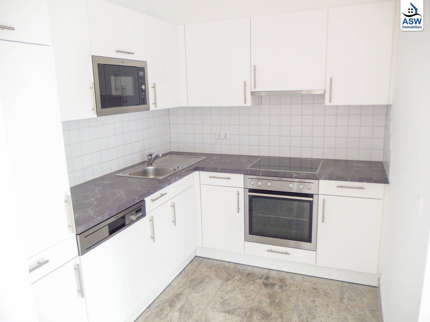Moderne weiße Einbauküche mit dunkler Arbeitsplatte und integrierten Elektrogeräten.