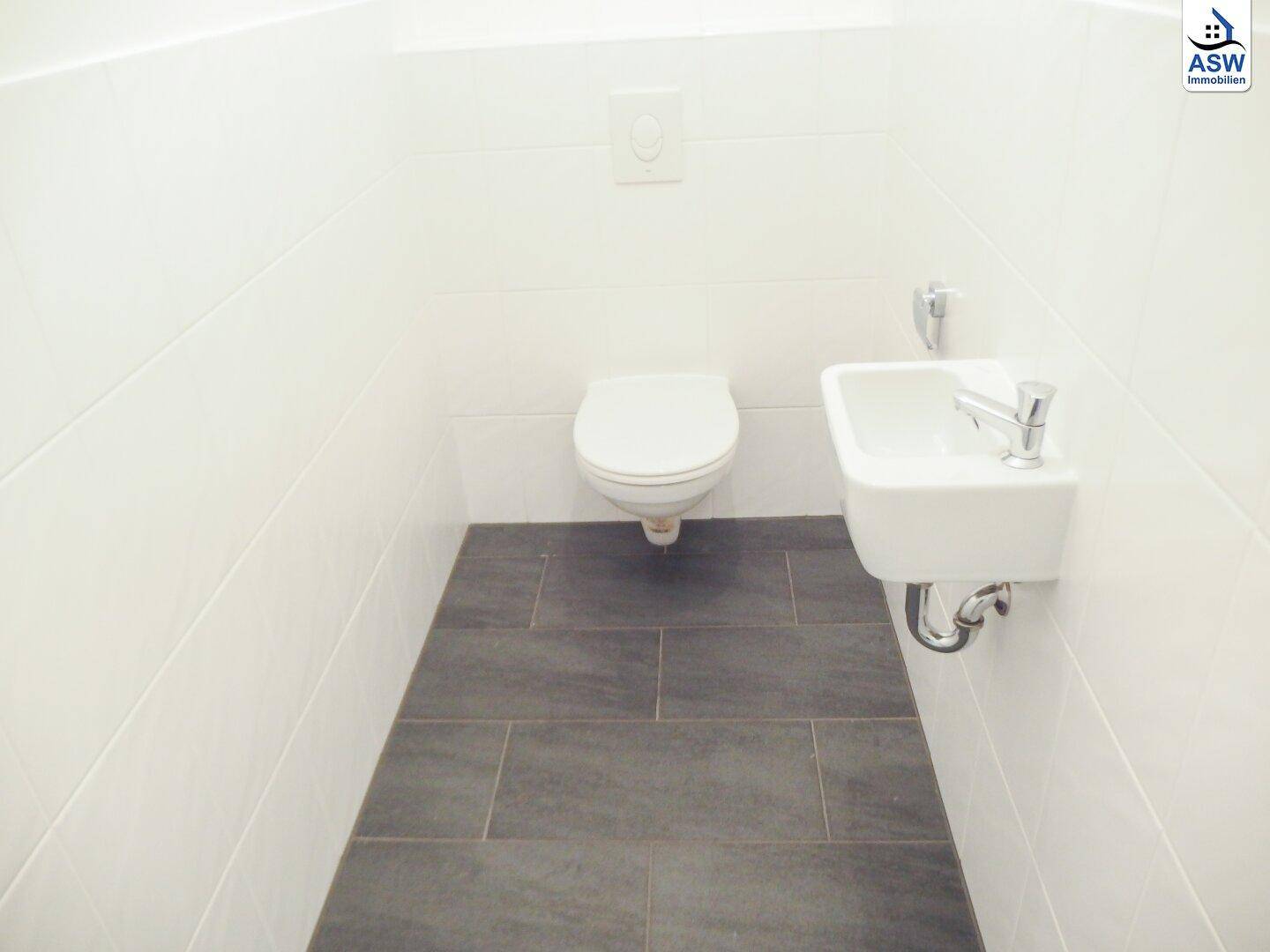 Modernes Gäste-WC mit dunklen Bodenfliesen und wandhängendem WC.
