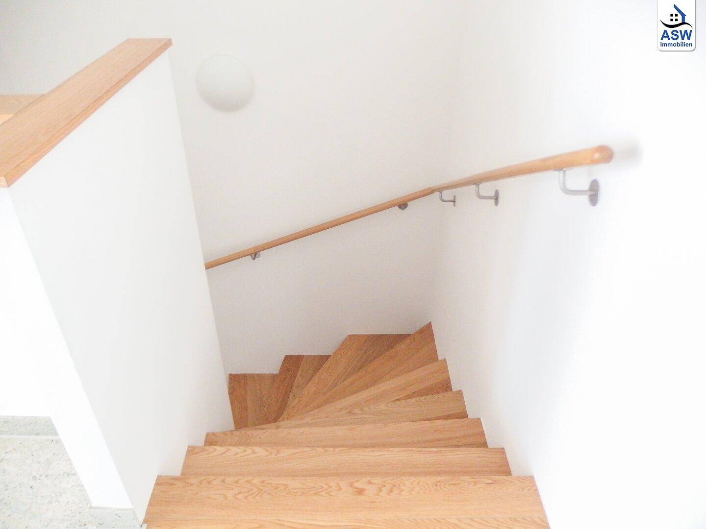 Helle Holztreppe mit Handlauf, die in die obere Etage führt.