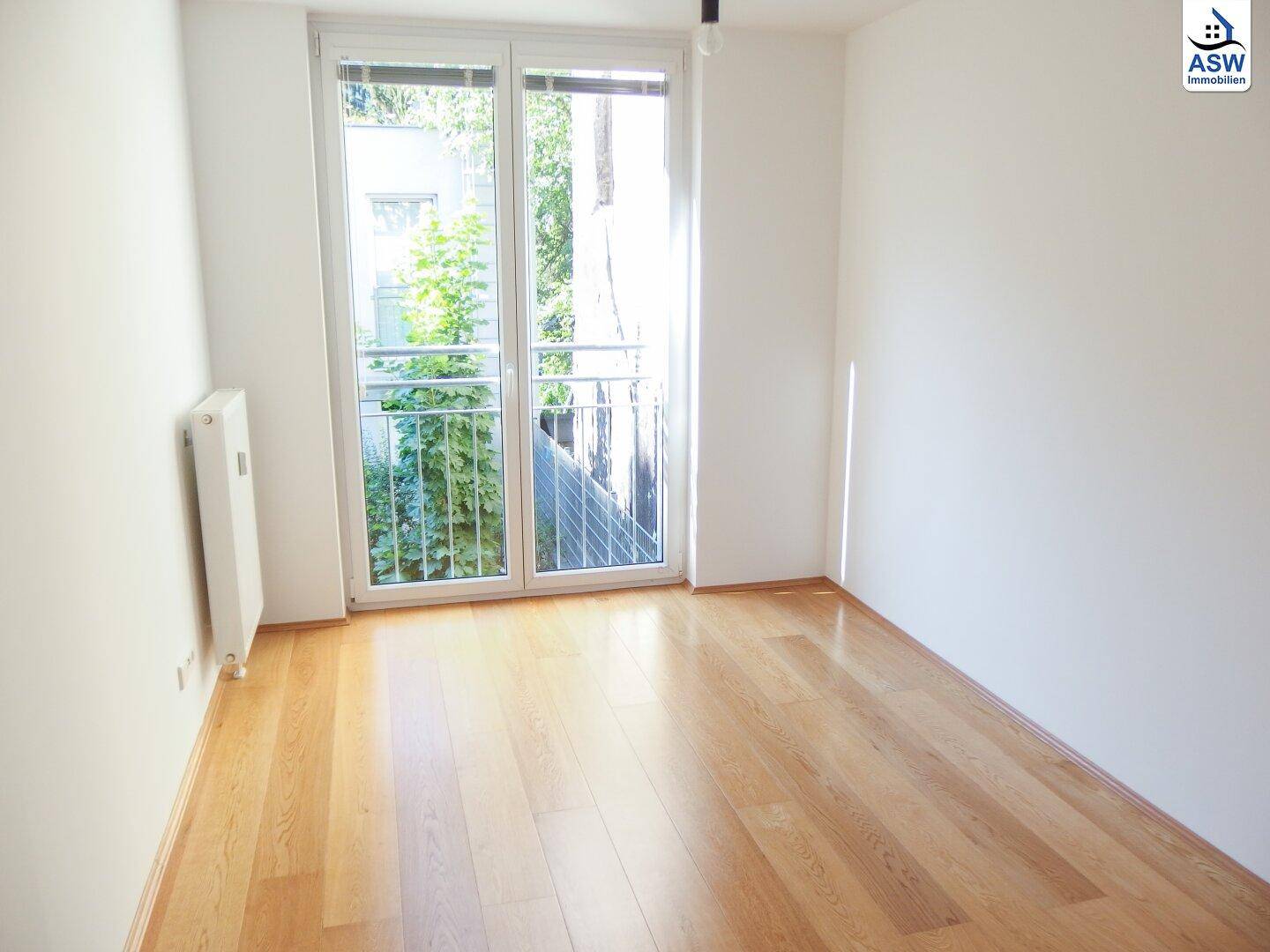 Helles Zimmer mit Holzboden und Zugang zu einem französischen Balkon.