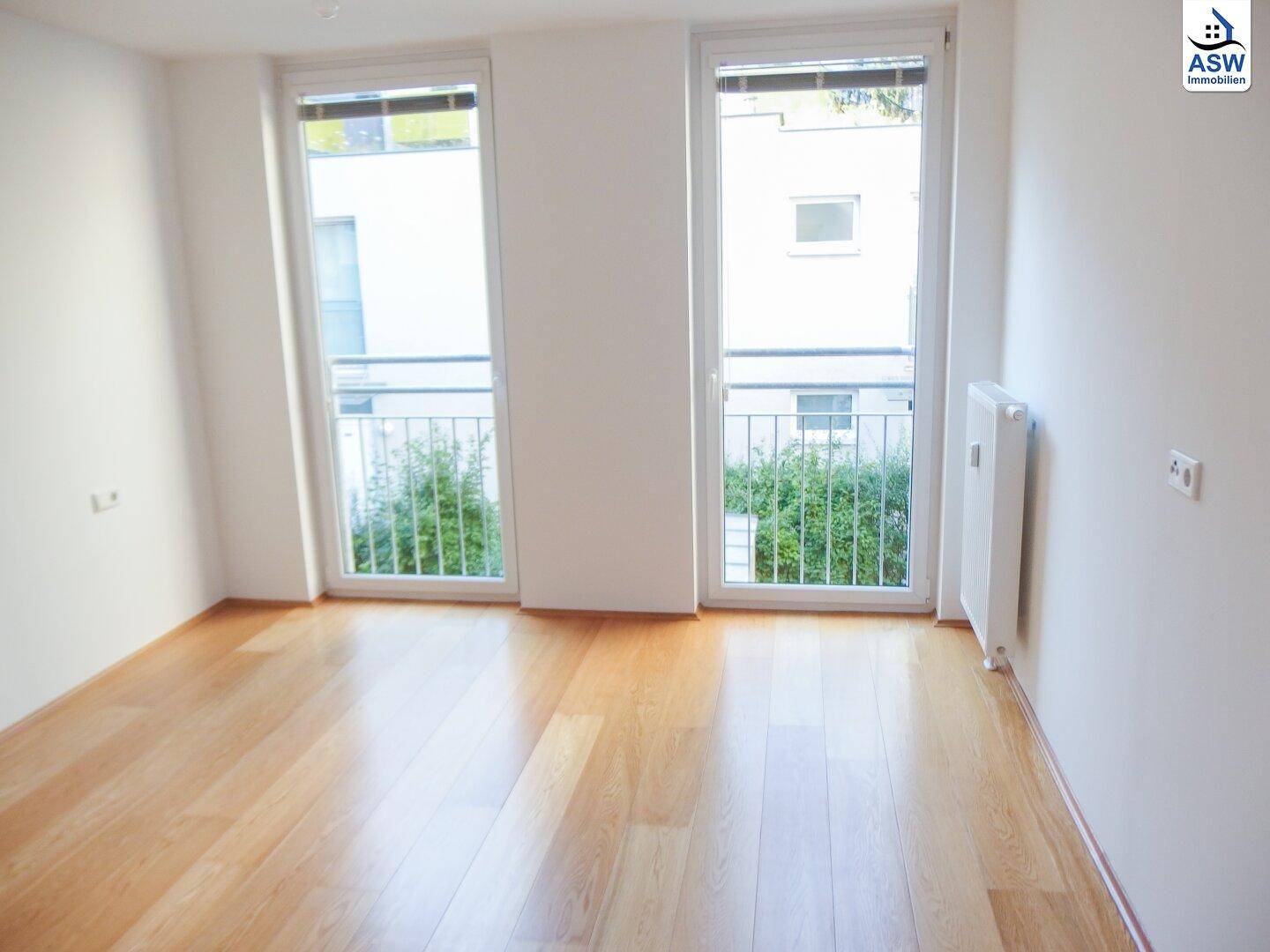 Helles Zimmer mit Holzboden und zwei französischen Balkonen.