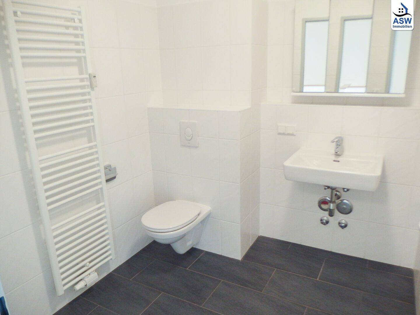 Modernes Badezimmer mit weißen Fliesen, dunklem Boden und Handtuchheizkörper.