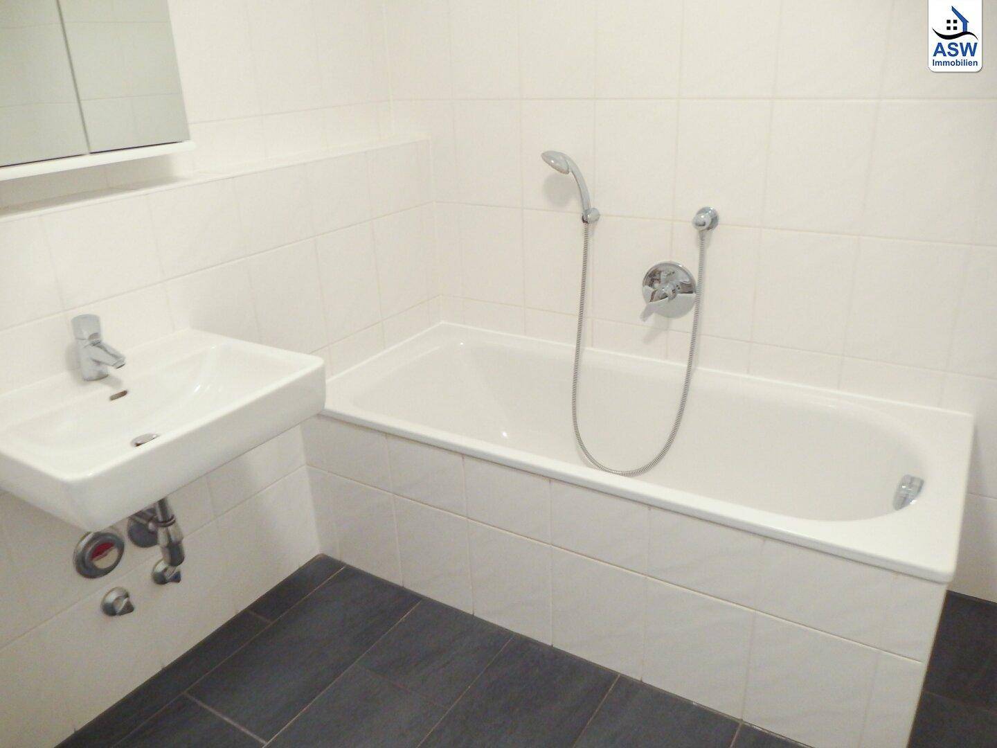 Modernes Badezimmer mit Badewanne, Waschbecken und dunklen Bodenfliesen.