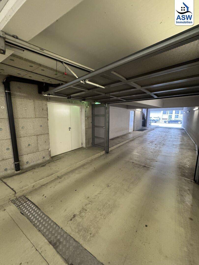Einfahrt zu einer Tiefgarage mit Rampe, mehreren Lagereinheiten und sichtbaren Garagentoren.