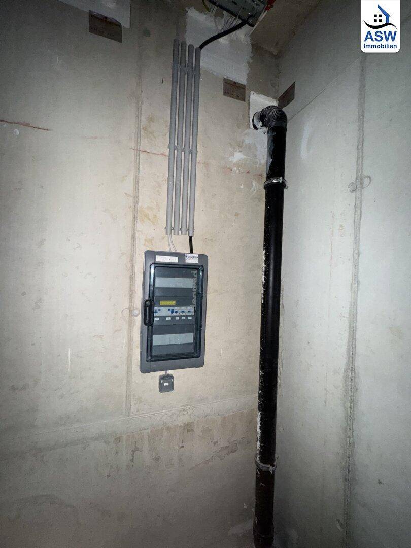 Detailansicht eines Technikbereichs im Keller mit einem Sicherungskasten und einer vertikalen Abwasserleitung.
