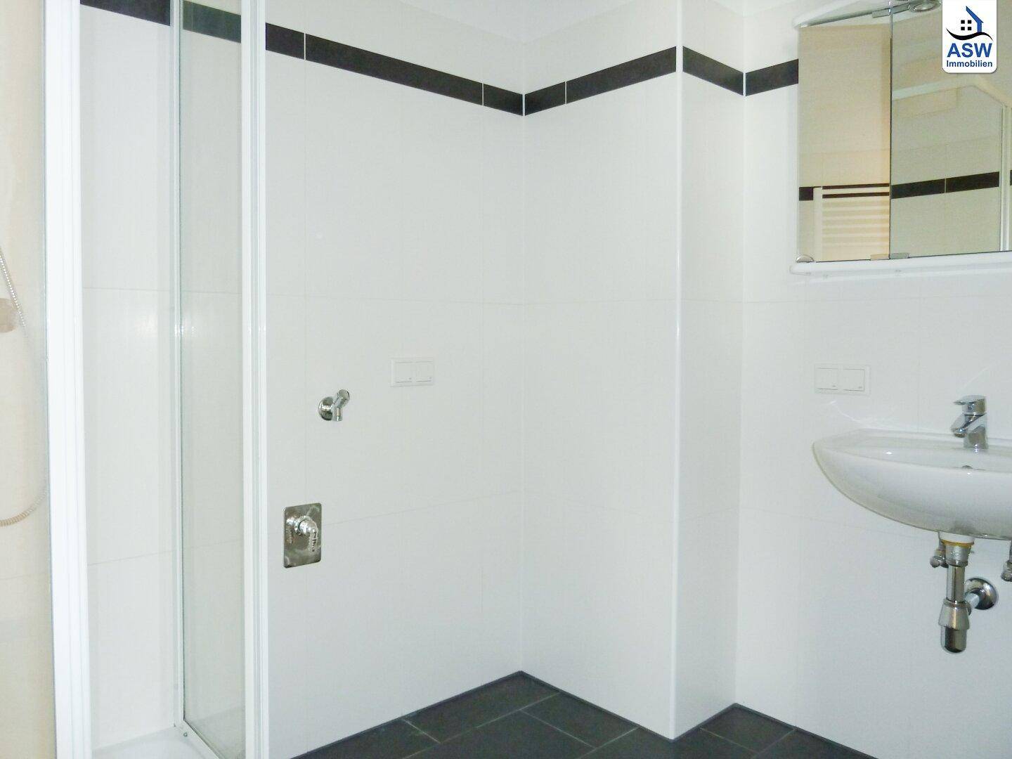 Modernes Badezimmer mit weiß gefliesten Wänden, dunklem Fliesenboden und einer Duschkabine.