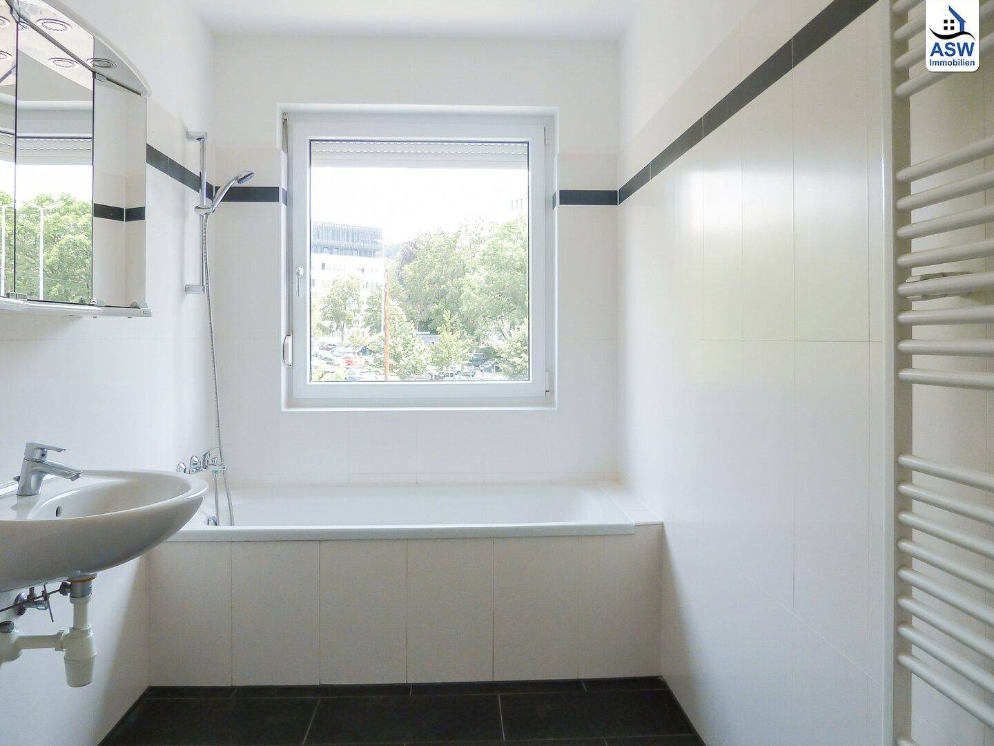 Modernes Badezimmer mit Badewanne, Einzelwaschbecken, Fenster und beheiztem Handtuchhalter.