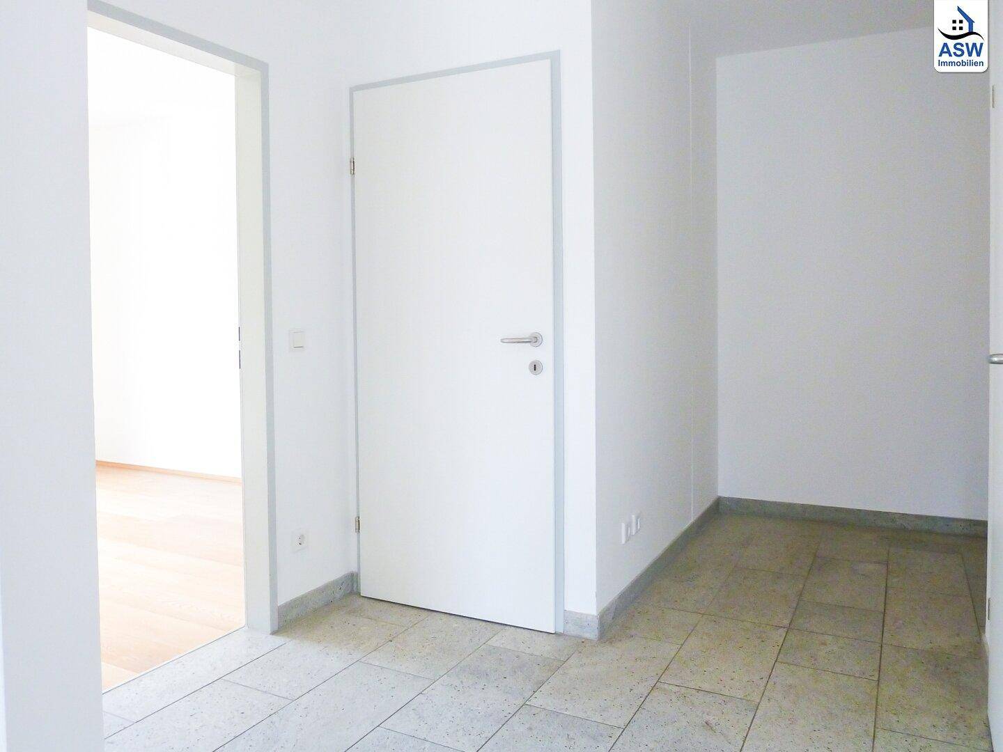Eingangsbereich mit Fliesenboden und weißer Tür, die zu einem der Zimmer führt.